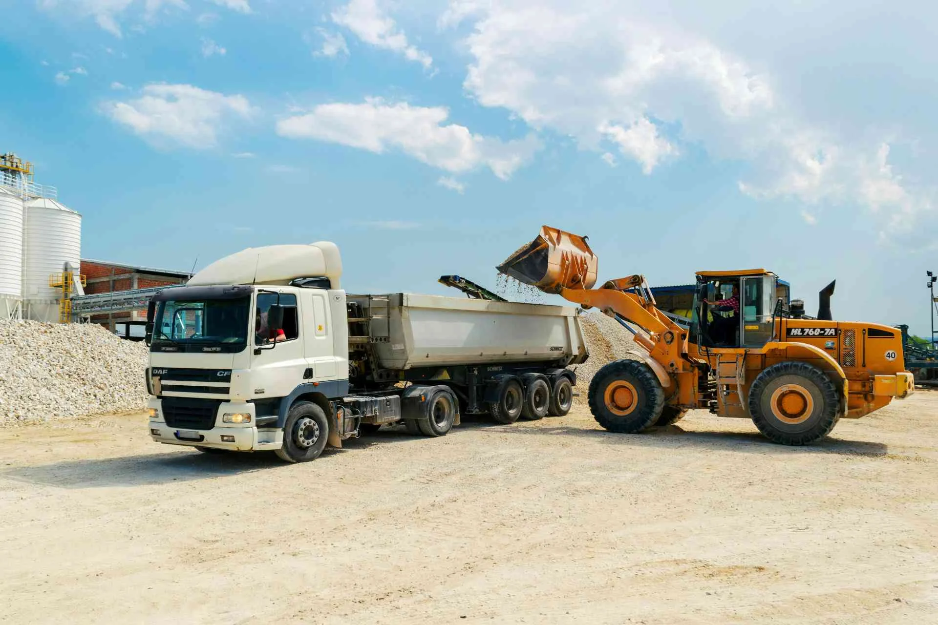 Ảnh phong cảnh chill tại khu khai thác đá với xe ben trắng và máy xúc màu cam dưới bầu trời xanh