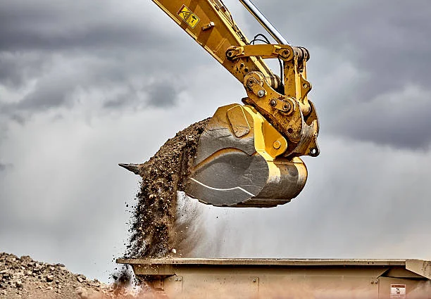 Gầu máy xúc đang đổ đất trong công trường dưới trời nhiều mây