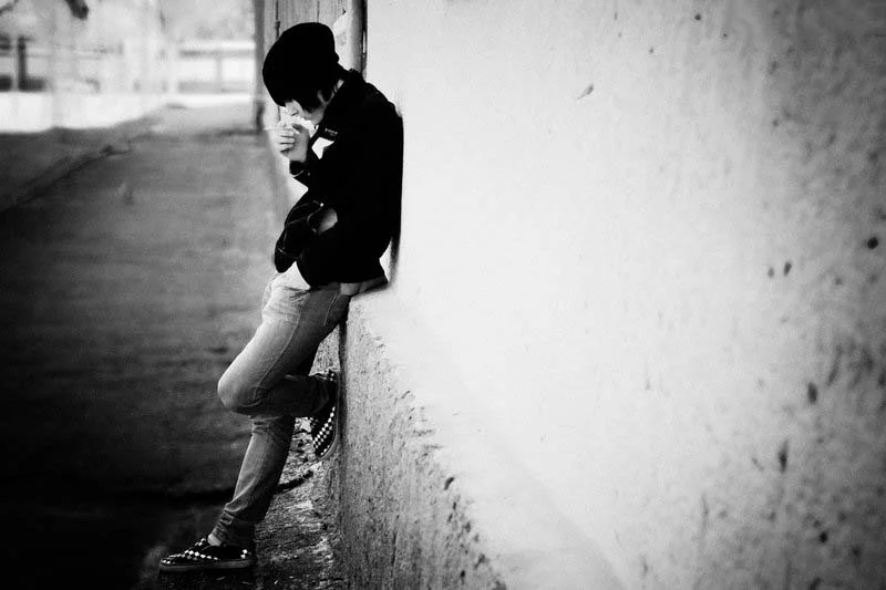 Người ngồi tựa vào bức tường trong ảnh đen trắng, mang vẻ cô đơn và suy tư