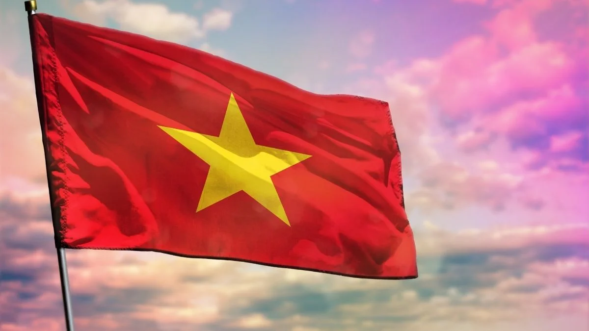 Ảnh lá cờ Việt Nam màu đỏ sao vàng tung bay trên nền trời hoàng hôn nhiều mây.