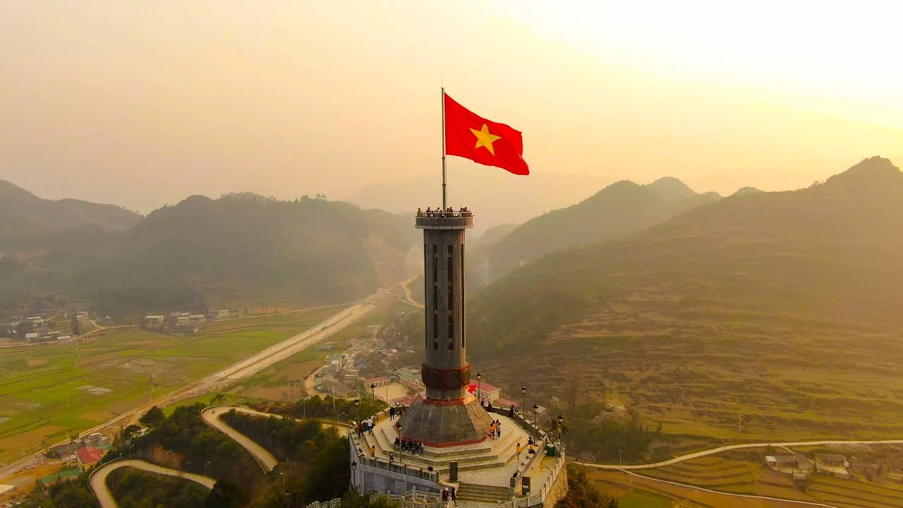 Lá cờ Việt Nam tung bay trên tháp giữa khung cảnh núi non và thung lũng
