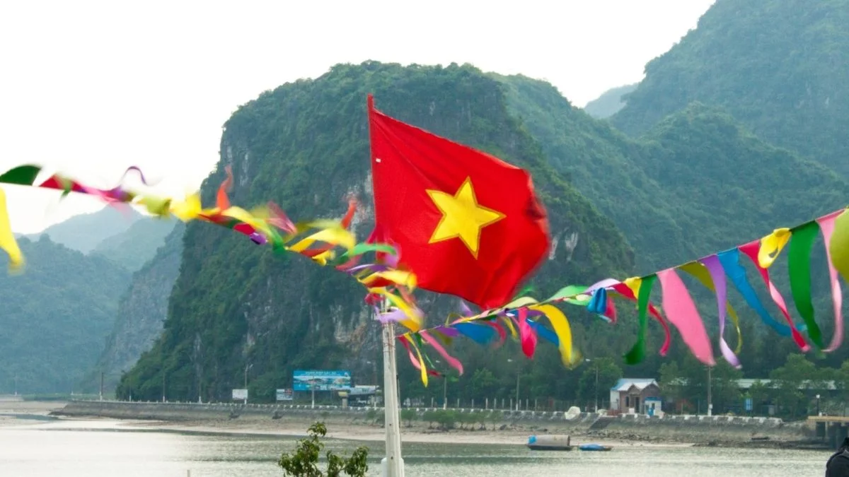 Lá cờ Việt Nam tung bay bên bờ nước với núi đá phía sau